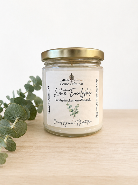 Candle jar with a label on a wooden surface with eucalyptus leaves.
