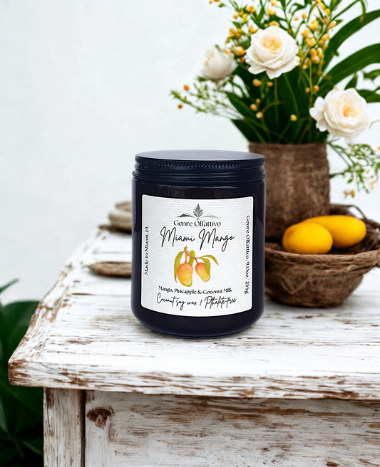 Candle labeled 'Miami Mango' on a wooden surface with flowers and fruits in the background