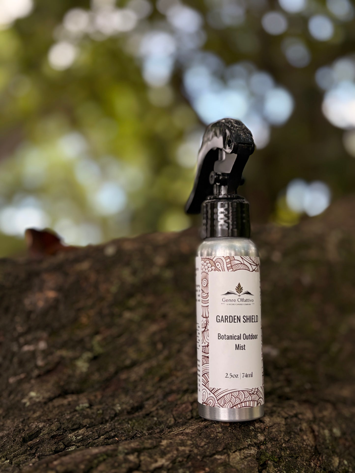 A small spray bottle labeled 'Garden Shield Botanical Garden Mist' by Clover Crafts, placed on a textured tree trunk with a blurred outdoor background of green foliage.