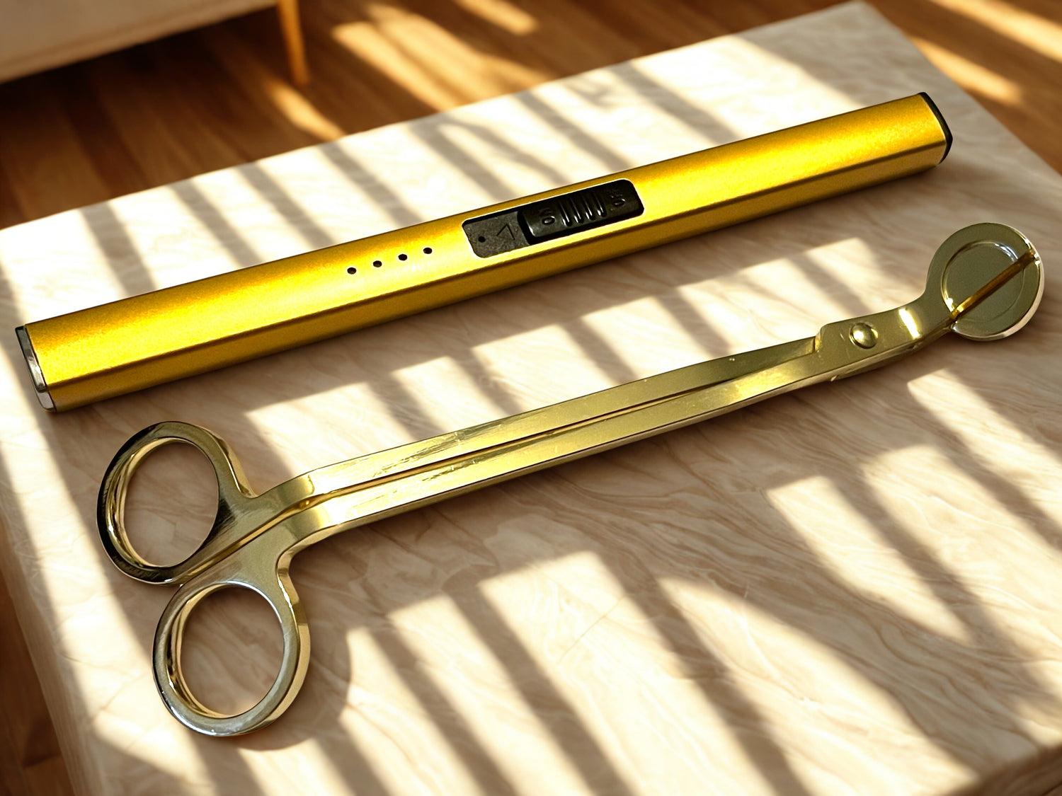Gold-colored scissors and a similar tool on a wooden surface with sunlight casting shadows.
